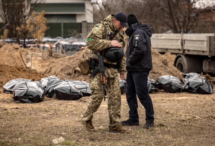 A member of the Ukrainian army and a policeman stand near body bags exhumed from a mass grave where civilians where buried in Bucha, on the outskirts of Kyiv, on April 13, 2022, amid Russia's military invasion launched on Ukraine. (Getty Images)