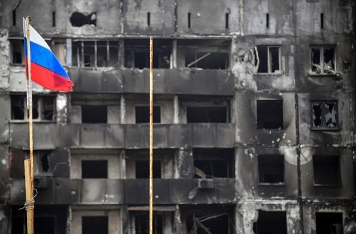 A Russian national flag flies in front of buildings destroyed by Russian forces in the war-ravaged city of Mariupol, southeastern Ukraine. (Photo by Alexander Nemenov/AFP via Getty Images)