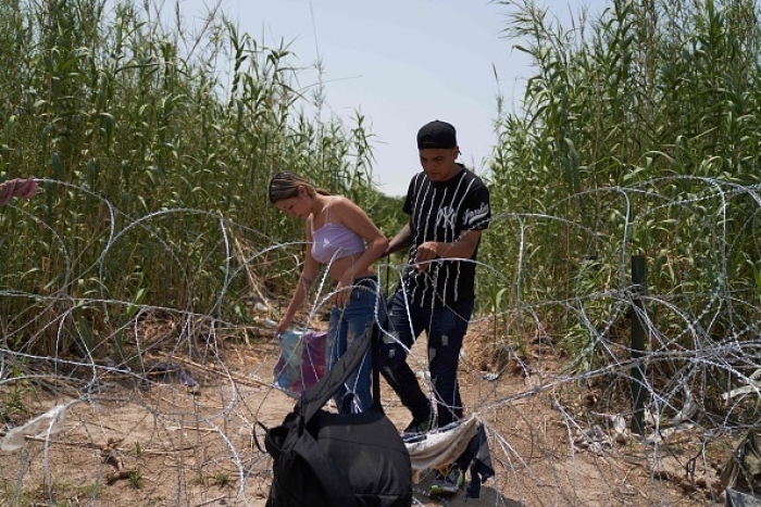 Migrants who illegally crossed the Rio Grande River climb through concertina wire in Eagle Pass, Texas, on May 22, 2022. (Photo by ALLISON DINNER/AFP via Getty Images)
