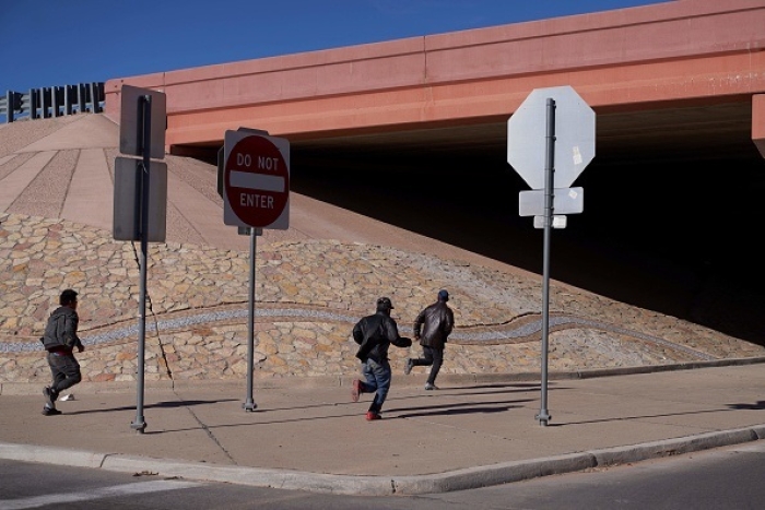 Migrants run into the street to evade law enforcement after illegally crossing into the US via a hole in a fence in El Paso, Texas, on December 22, 2022. (Photo by ALLISON DINNER/AFP via Getty Images)