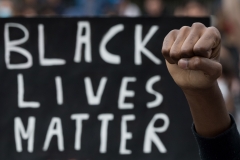 A protester raises a fist next to a Black Lives Matter placard. (Photo credit: LOIC VENANCE/AFP via Getty Images)