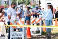 A COVID-19 test site volunteer wearing personal protective equipment speaks with people waiting in line at a walk-in coronavirus test site in Los Angeles, California on July 10, 2020. (Photo by FREDERIC J. BROWN/AFP via Getty Images)