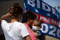 Migrants are seen with a US President Joe Biden campaign flag in the background at a camp where asylum seekers wait for US authorities to allow them to start their migration process outside El Chaparral crossing port in Tijuana, Baja California state, Mexico on March 17, 2021. (Photo by GUILLERMO ARIAS/AFP via Getty Images)