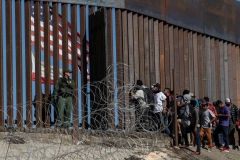 Central American migrants look through a border fence as a US Border PatRol agents stands guard near the El Chaparral border crossing in Tijuana, Baja California State, Mexico, on November 25, 2018. (Photo by GUILLERMO ARIAS/AFP via Getty Images)